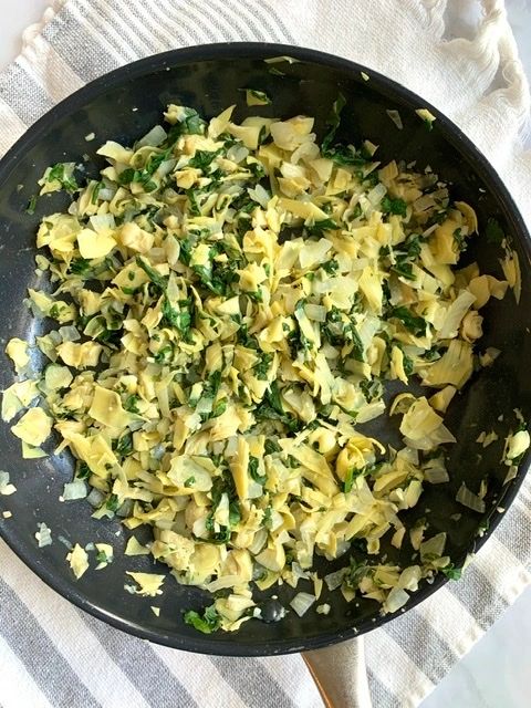 process photo of onions, garlic, artichoke hearts and spinach in a pan 