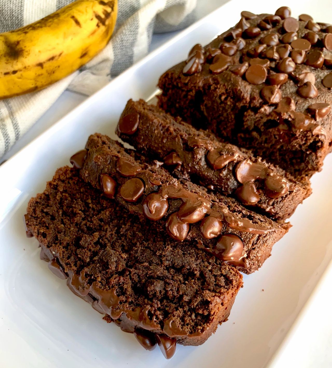 vegan chocolate banana bread on a white plate next to a banana 