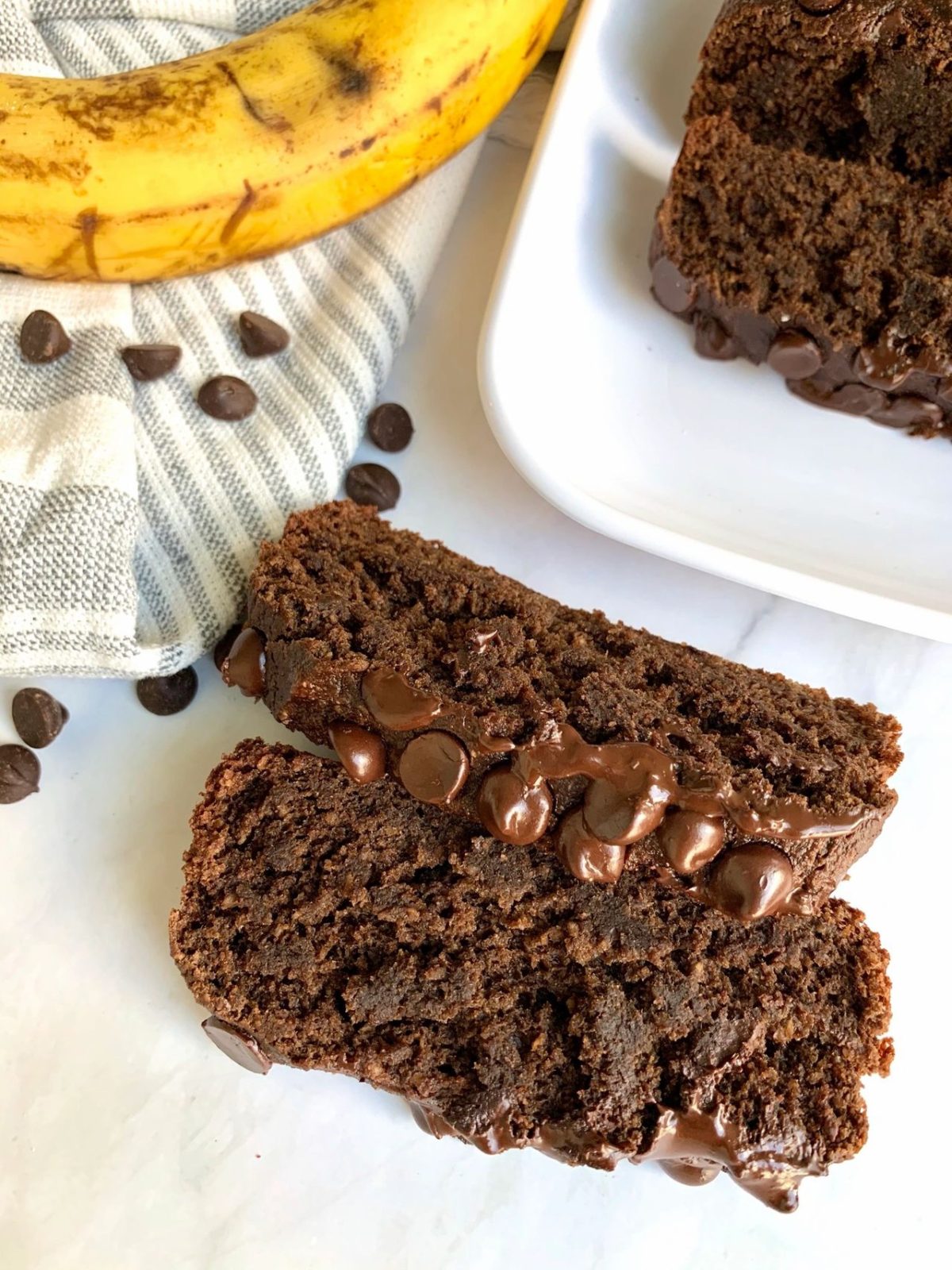 two slices of vegan chocolate banana bread next to a banana and chocolate chips 