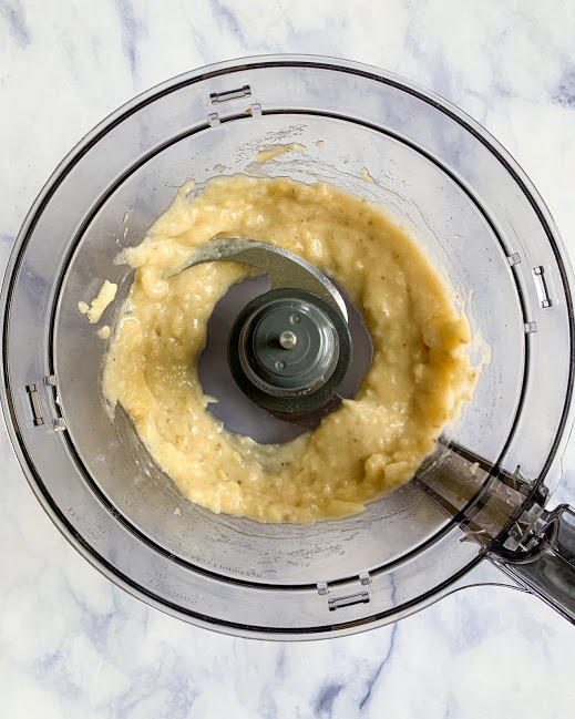 mashed banana in a food processor on a white background 