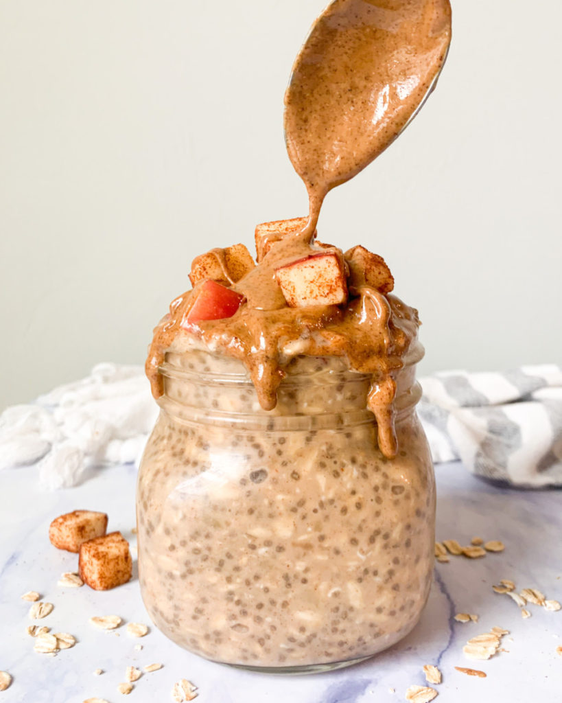 vertical photo of vegan apple & almond butter overnight oats in a jar on a white marble counter top 