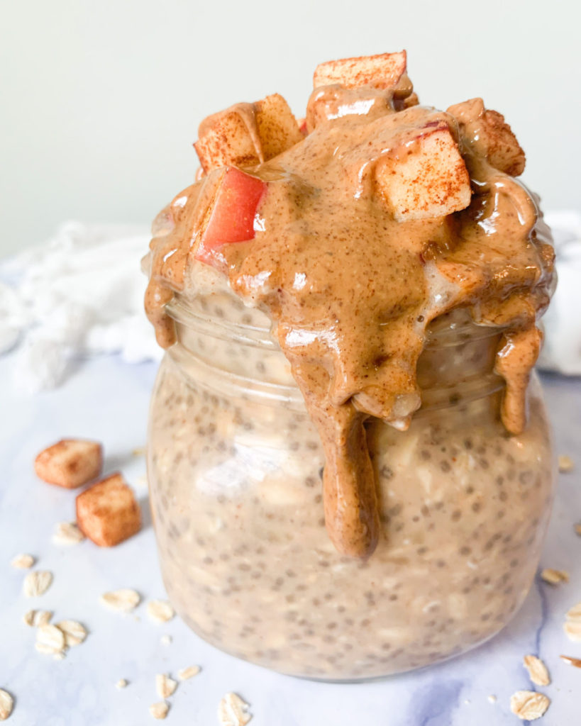 vertical photo of vegan apple & almond butter overnight oats in a jar on a white marble counter top 