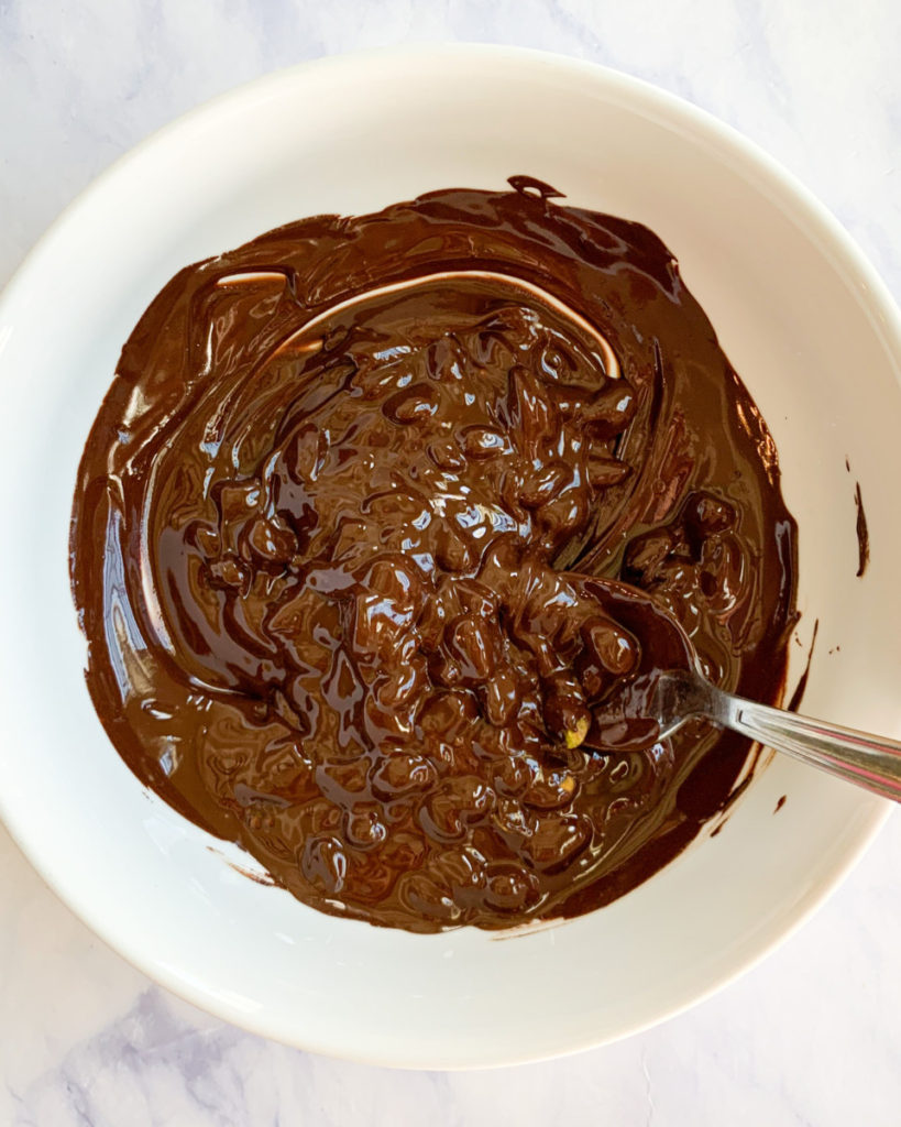 process photo of melted dark chocolate in a white bowl on a white counter top 