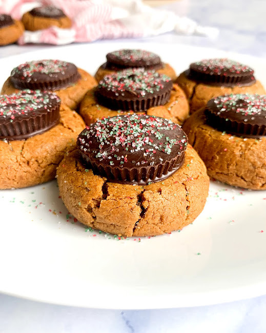 a vertical image of vegan flourless peanut butter cup blossoms on a white plate on a white counter top with cookies and a red and white napkin in the background 