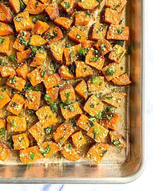 a vertical image of vegan savory roasted sweet potatoes with parsley and green onion on a baking sheet 