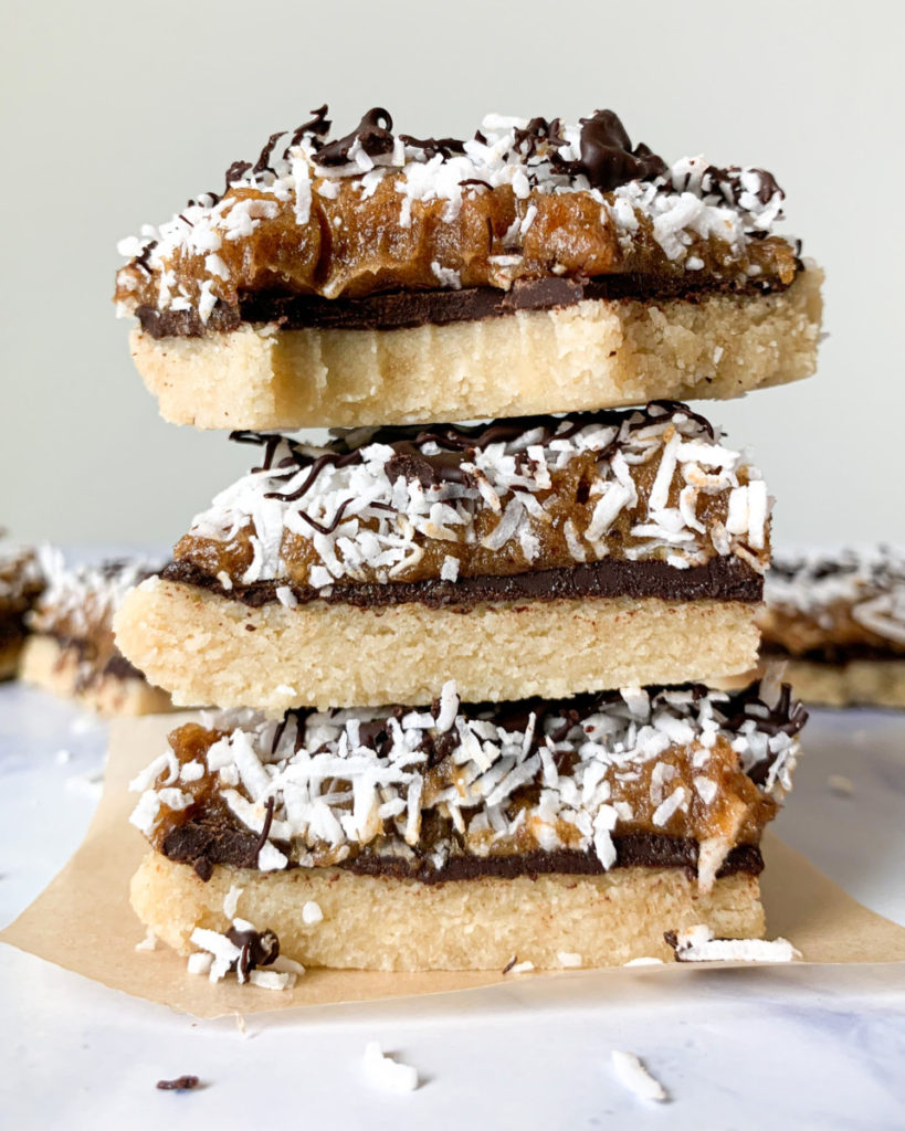 a vertical image of healthier vegan no bake samoa bars stacked on top of each other on a white counter top with more bars in the background 