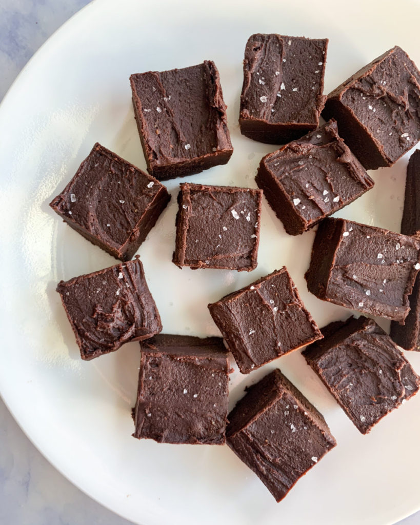 a vertical image of oil free vegan dark chocolate peanut butter fudge on a white plate on a white counter top 