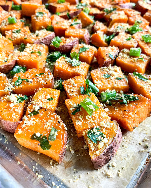 a vertical image of vegan savory roasted sweet potatoes with parsley and green onion on a baking sheet 