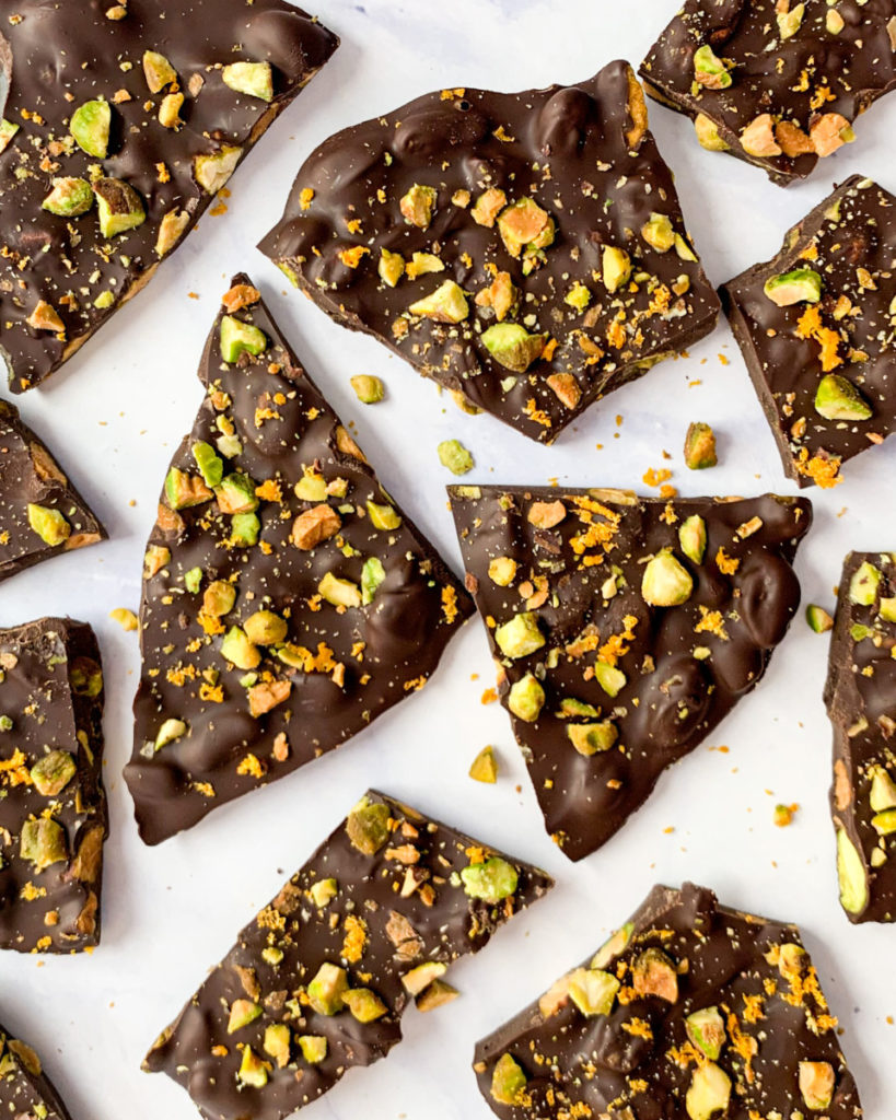 a vertical image of vegan dark chocolate pistachio and orange bark on a white counter top 