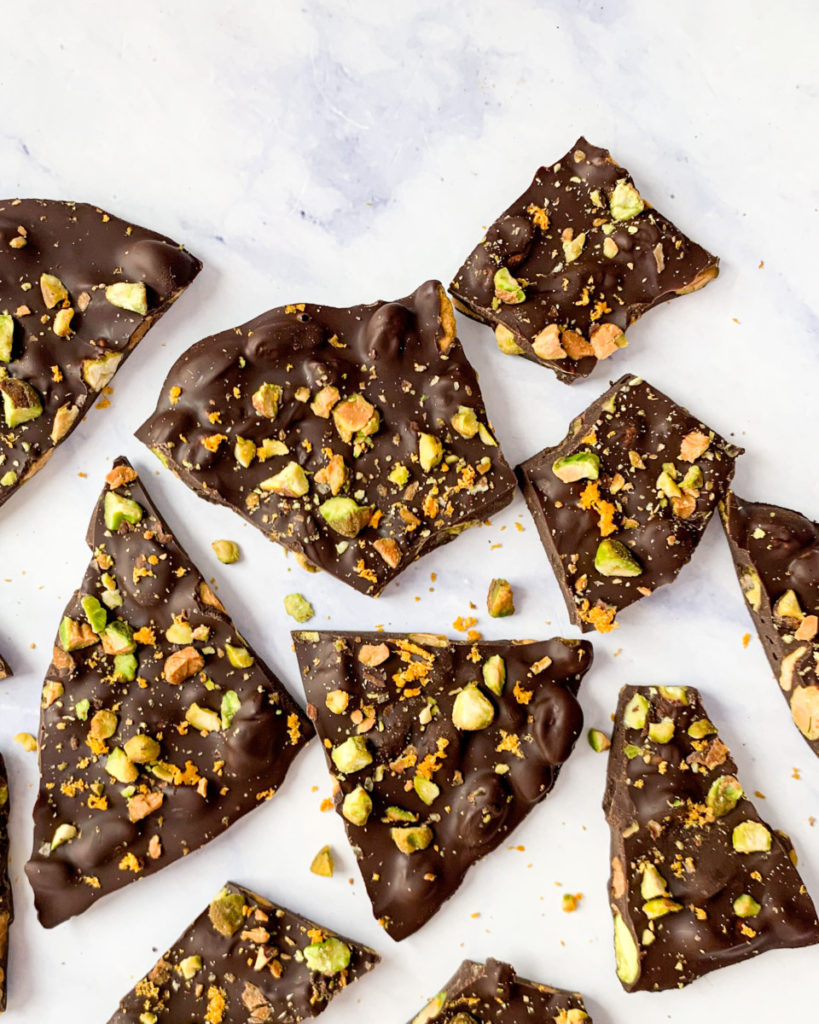 a vertical image of vegan dark chocolate pistachio and orange bark on a white counter top 