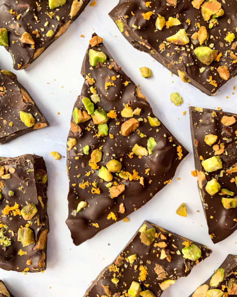 a vertical image of vegan dark chocolate pistachio and orange bark on a white counter top 