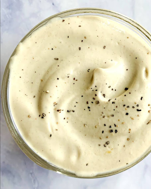 a vertical image of vegan Caesar salad dressing in a glass jar on a white counter top 