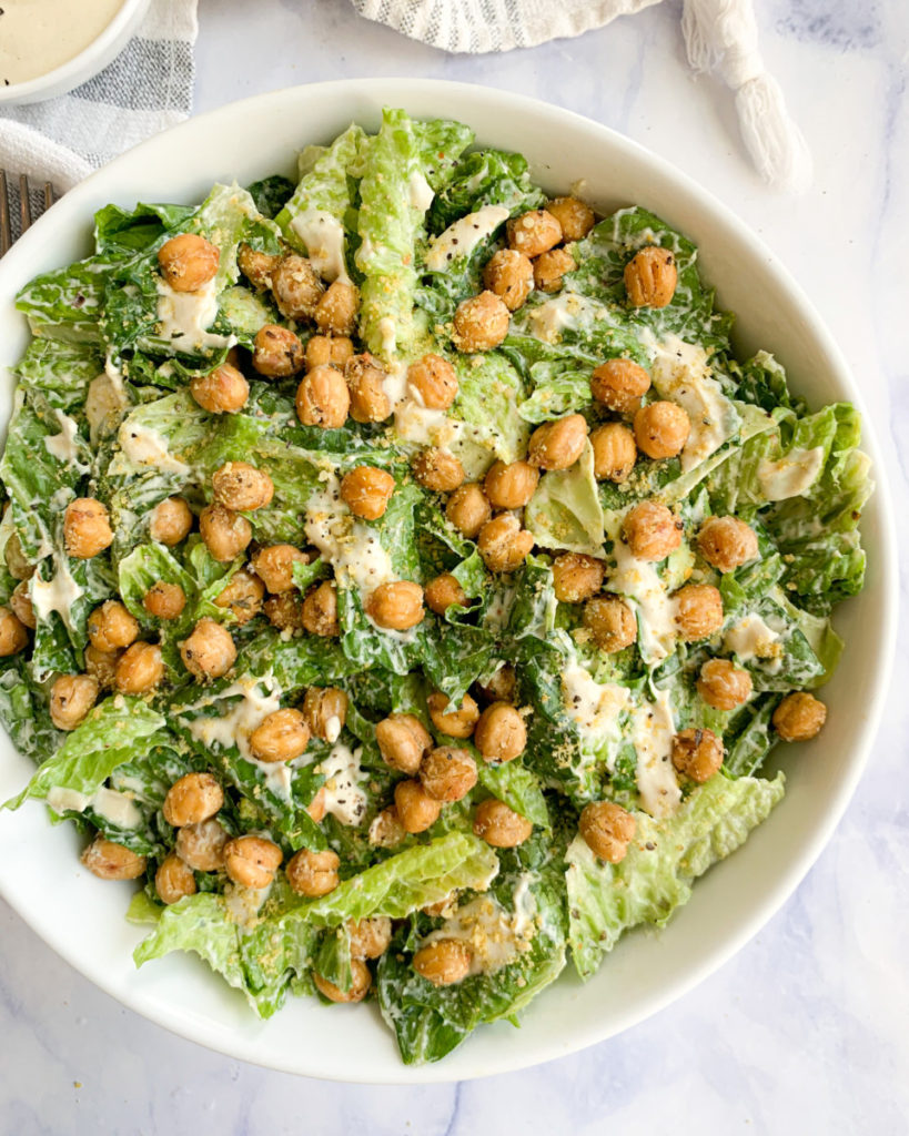 a vertical image of vegan Caesar salad with crispy chickpea croutons in a white bowl on a white counter top 