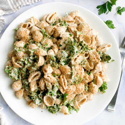 a vertical image of easy vegan creamy walnut pasta with homemade italian breadcrumbs on a white plate with a blue and white napking and breadcrumbs in the background