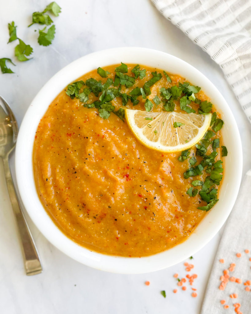 creamy vegan red lentil soup in a bowl topped with cilantro and lemon on a white counter top 