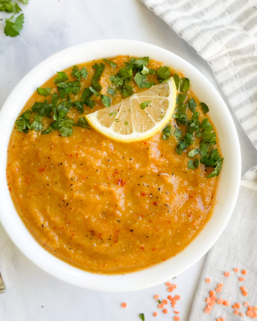 oil free vegan red lentil soup in a bowl topped with cilantro and lemon on a white counter top 