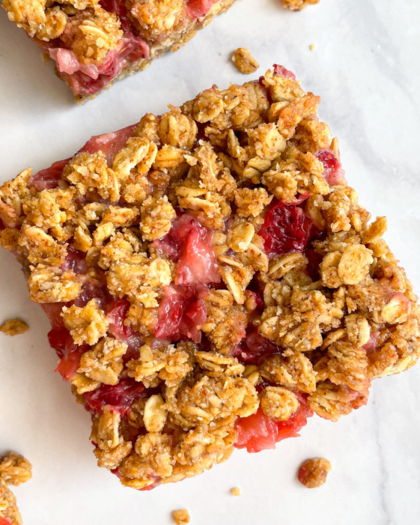 a close up photos of no bake vegan strawberry almond oat bars on a white counter top 