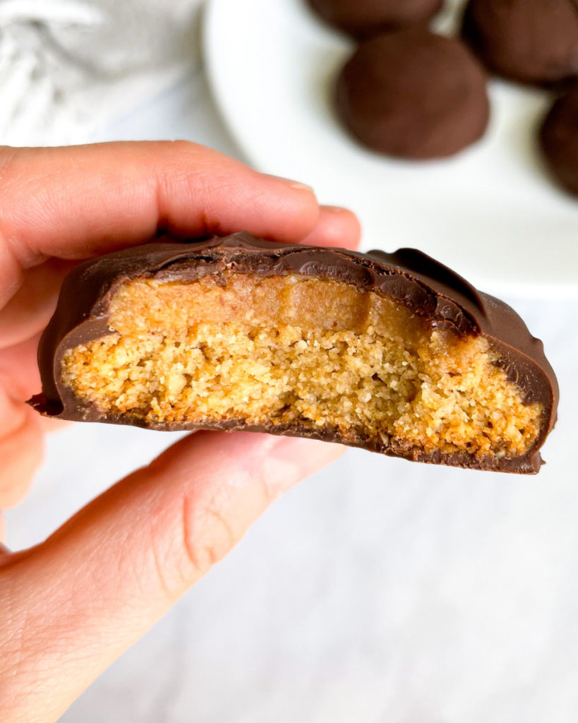 a hand holding oil-free gluten-free healthier vegan tagalongs with more tagalongs in the background  on a white plate 