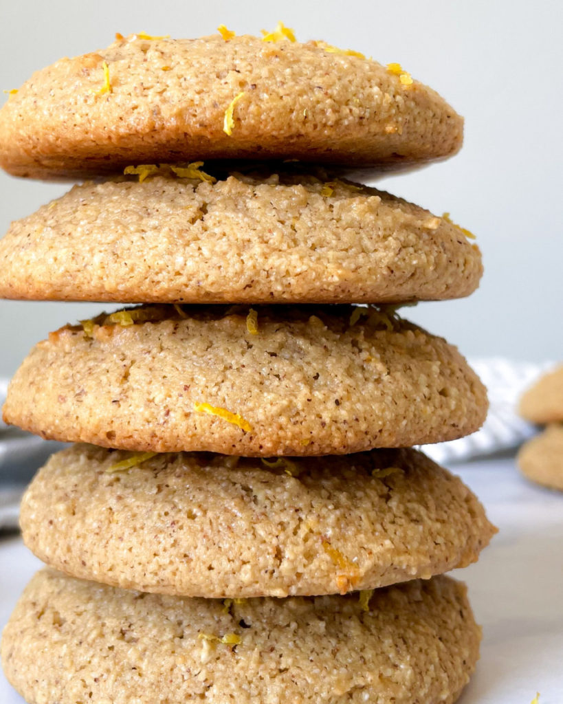 a close up image of 5 oil-free vegan lemon almond cookies stacked on a white counter top 