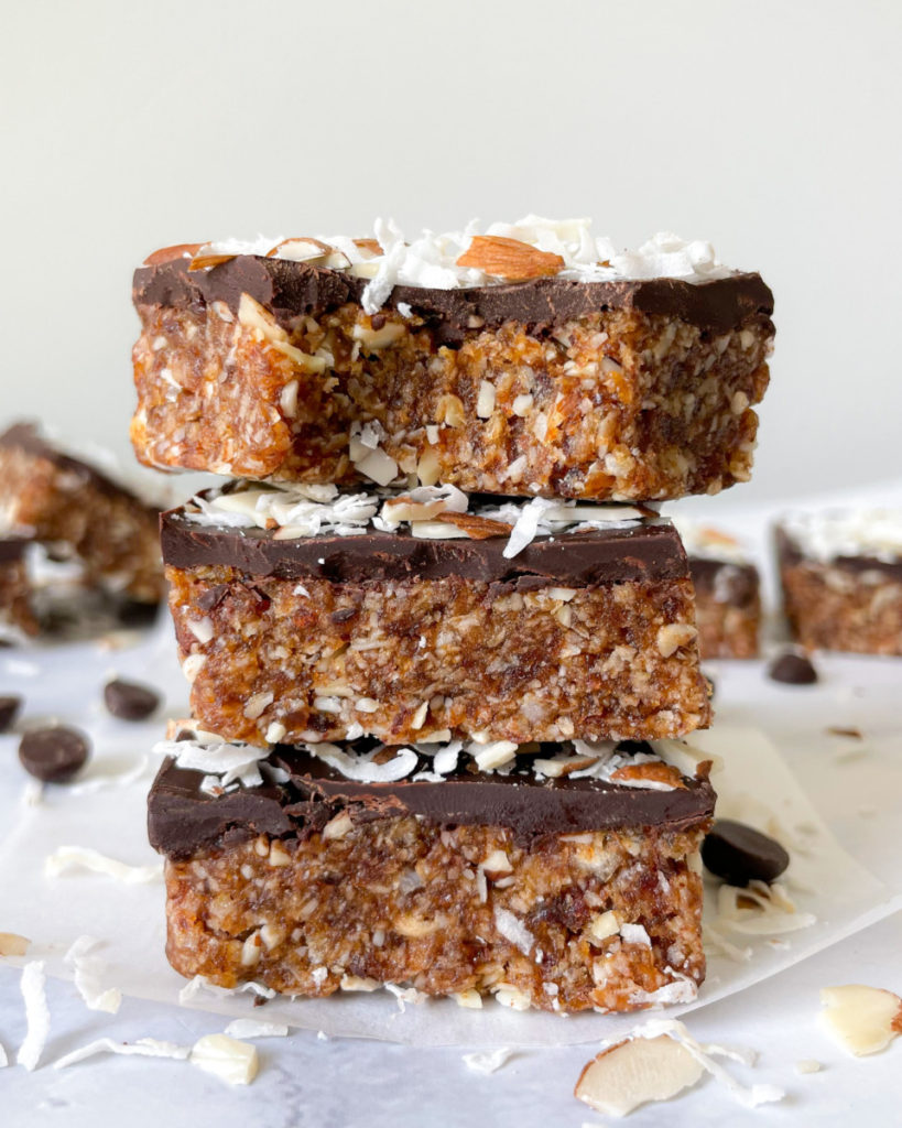 a photo of three date sweetened vegan no bake almond joy bars stacked on a white counter top with more bars in the background 