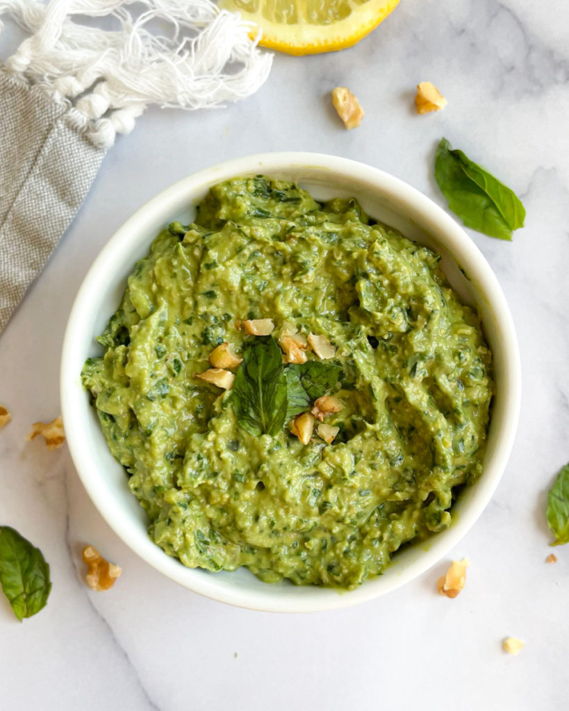 the best vegan oil-free pesto in a small white ramekin on a white counter top with basil and walnuts