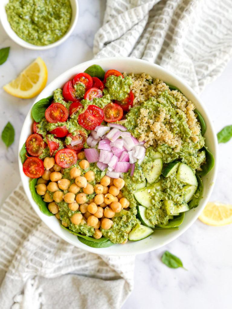 whole food plant based vegan oil-free pesto quinoa bowl with tomatoes, chickpeas, cucumbers and onions on a white counter top 