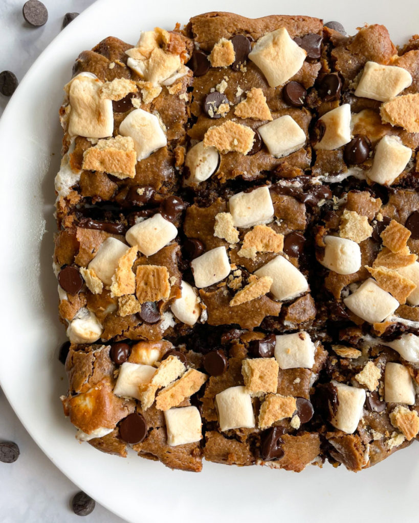 a close up photo of oil-free gluten-free vegan peanut butter s'mores bars topped with marshmallows, dark chocolate chips and graham crackers 