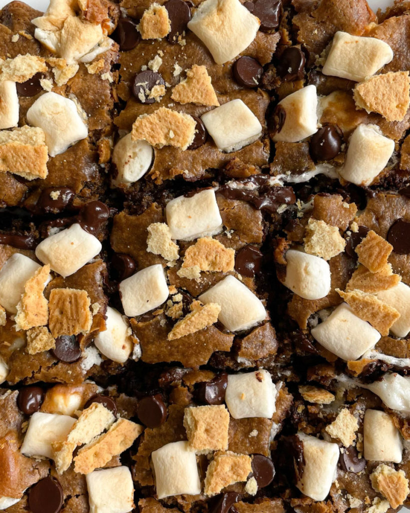 a close up photo of vegan peanut butter s'mores bars topped with marshmallows, dark chocolate chips and graham crackers 