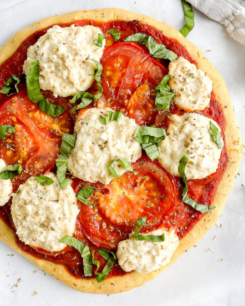 a close up photo of vegan oil-free chickpea and almond flour pizza crust with almond ricotta, tomatoes and basil 